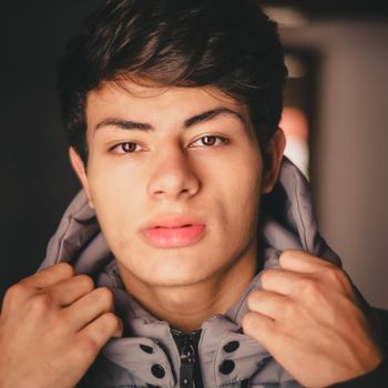 Close-up portrait of a young man adjusting his jacket indoors.