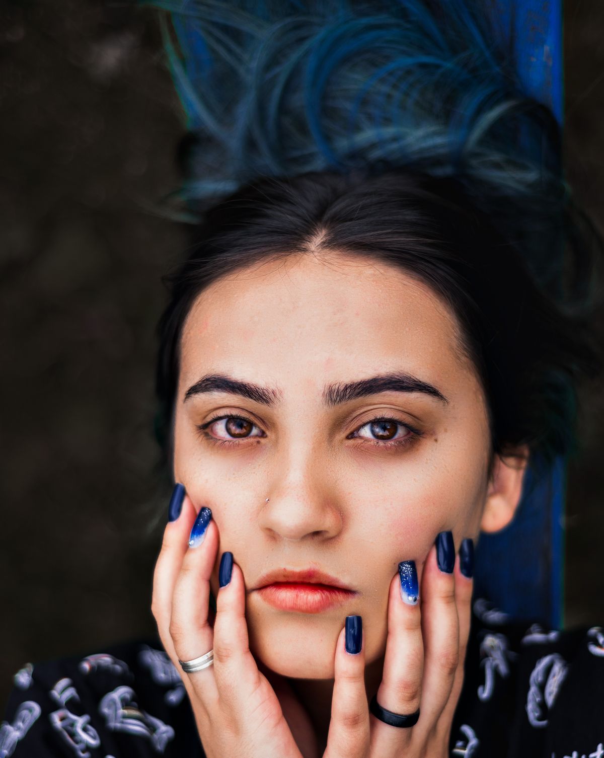 Intense close-up portrait of a woman with dark hair and striking blue nails.