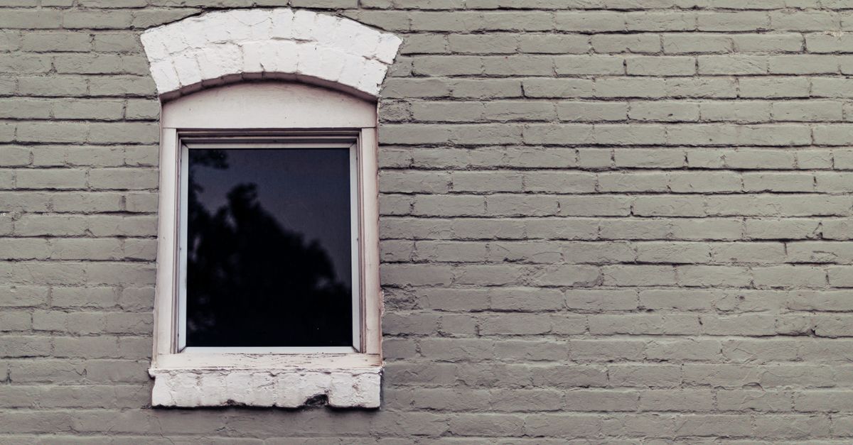 Exterior of old brick building of gray color with small window surrounded with white bricks in daylight