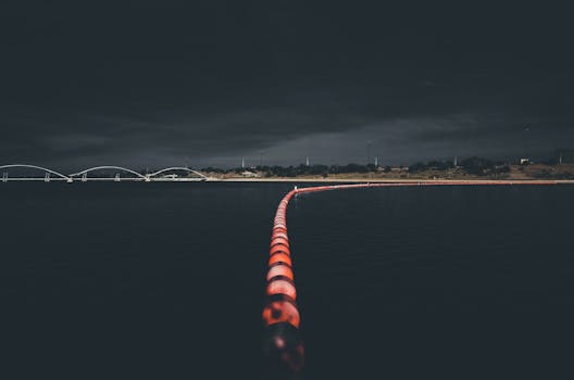 从上方俯瞰，现代桥梁附近的湖面上，照明浮标线漂浮在深色的水中，映衬着夜空