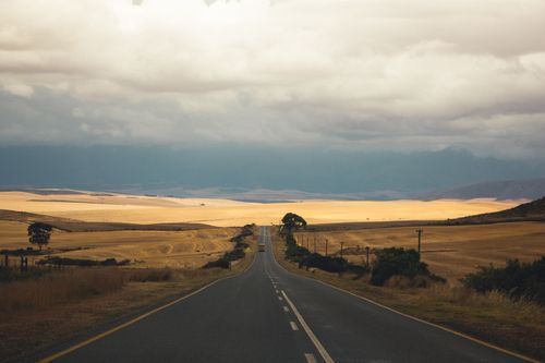 Free A tranquil rural road stretches through South African fields under a cloudy sky, capturing scenic beauty. Stock Photo