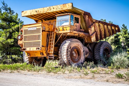 Weathered dump truck on sandy road near green trees in countryside