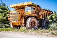 Weathered dump truck on sandy road near green trees in countryside