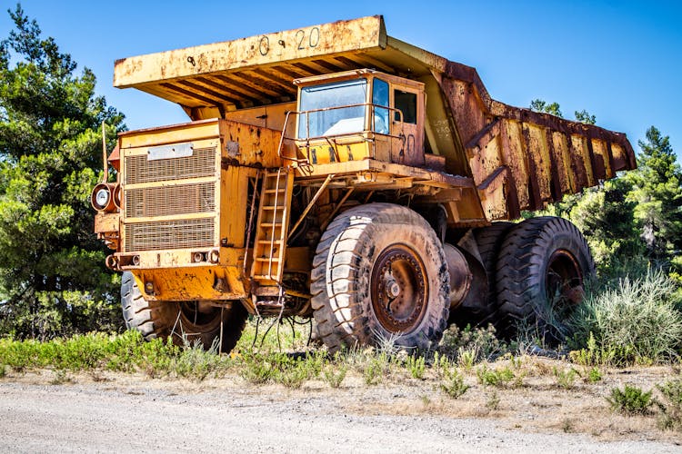 Weathered Dump Truck On Sandy Road Near Green Trees In Countryside