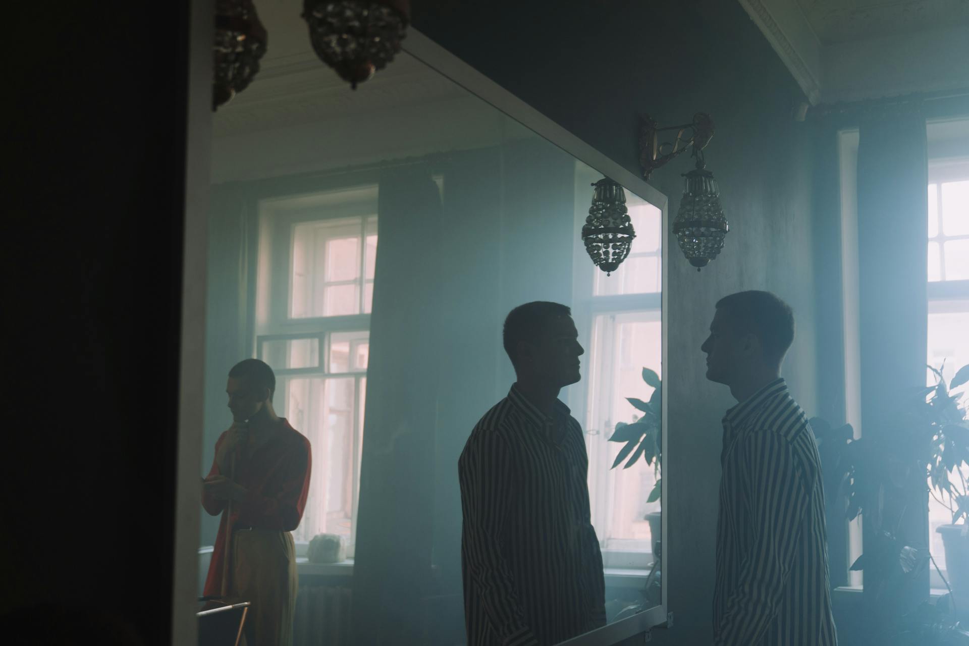 A man in striped shirt reflected in a mirror in a dimly lit room.