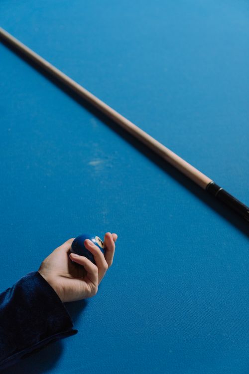 Free Close-up of hand holding billiard ball with cue stick on blue pool table. Stock Photo