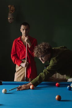 Two men playing billiards on a pool table in a dimly lit room, showcasing a leisure activity.