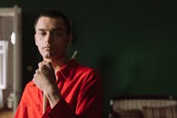 一位穿着红色衬衫、手持球杆的年轻人，在昏暗的室内自信地凝视着