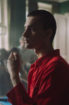 室内，一位穿着红色衬衫、戴着耳环的年轻人摆出精致的姿势，拍摄个人肖像
