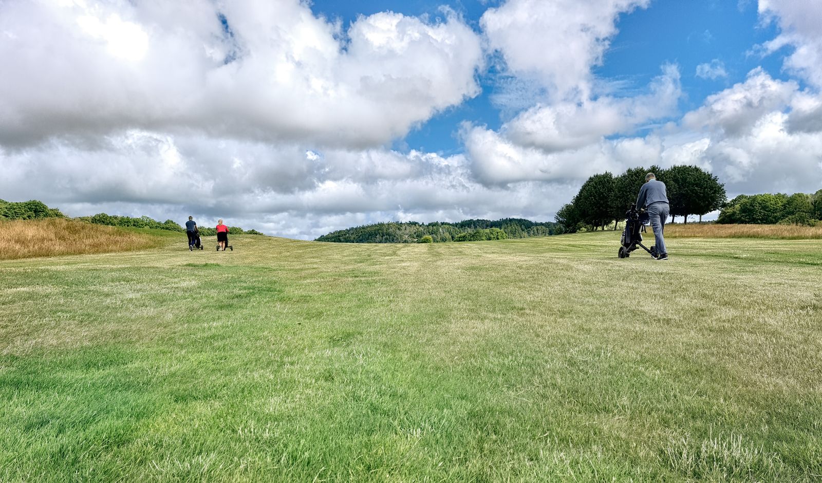 Two golfers pulling trolleys across a wide fairway under a big cloudy northern European sky