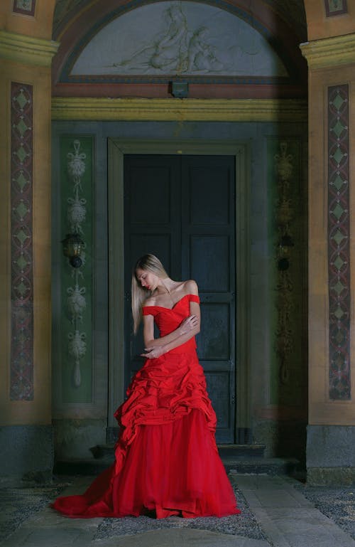 Elegant woman in red maxi dress standing in medieval palace