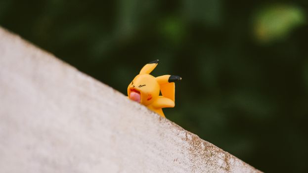 Vibrant yellow toy figurine playfully balancing on a ledge outdoors.