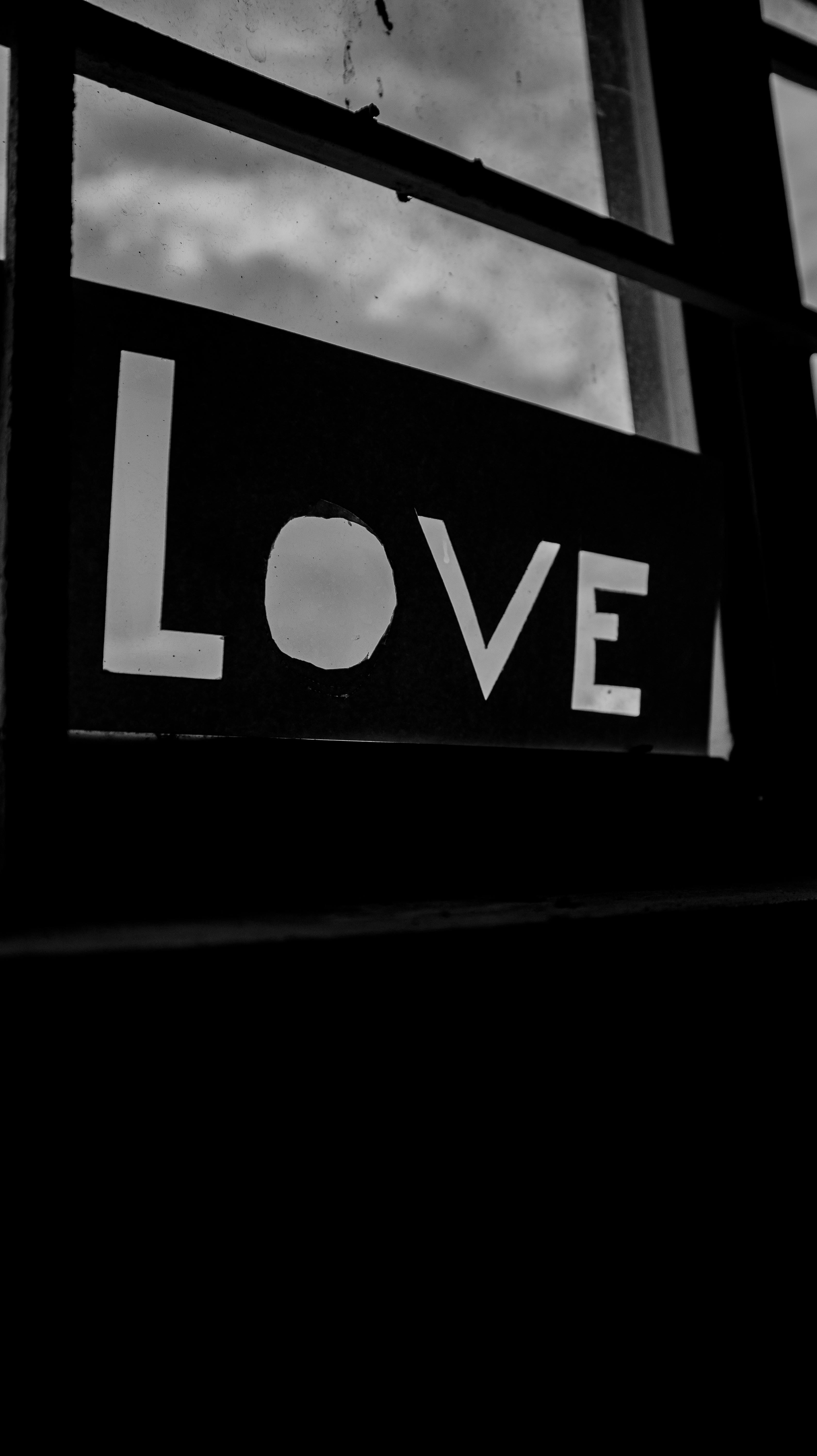 A minimalist black and white image of the word 'Love' cut out by a window.