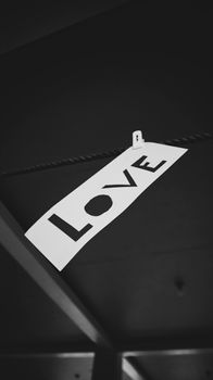 Grayscale photo of a paper sign with the word 'LOVE' hanging on a rope.