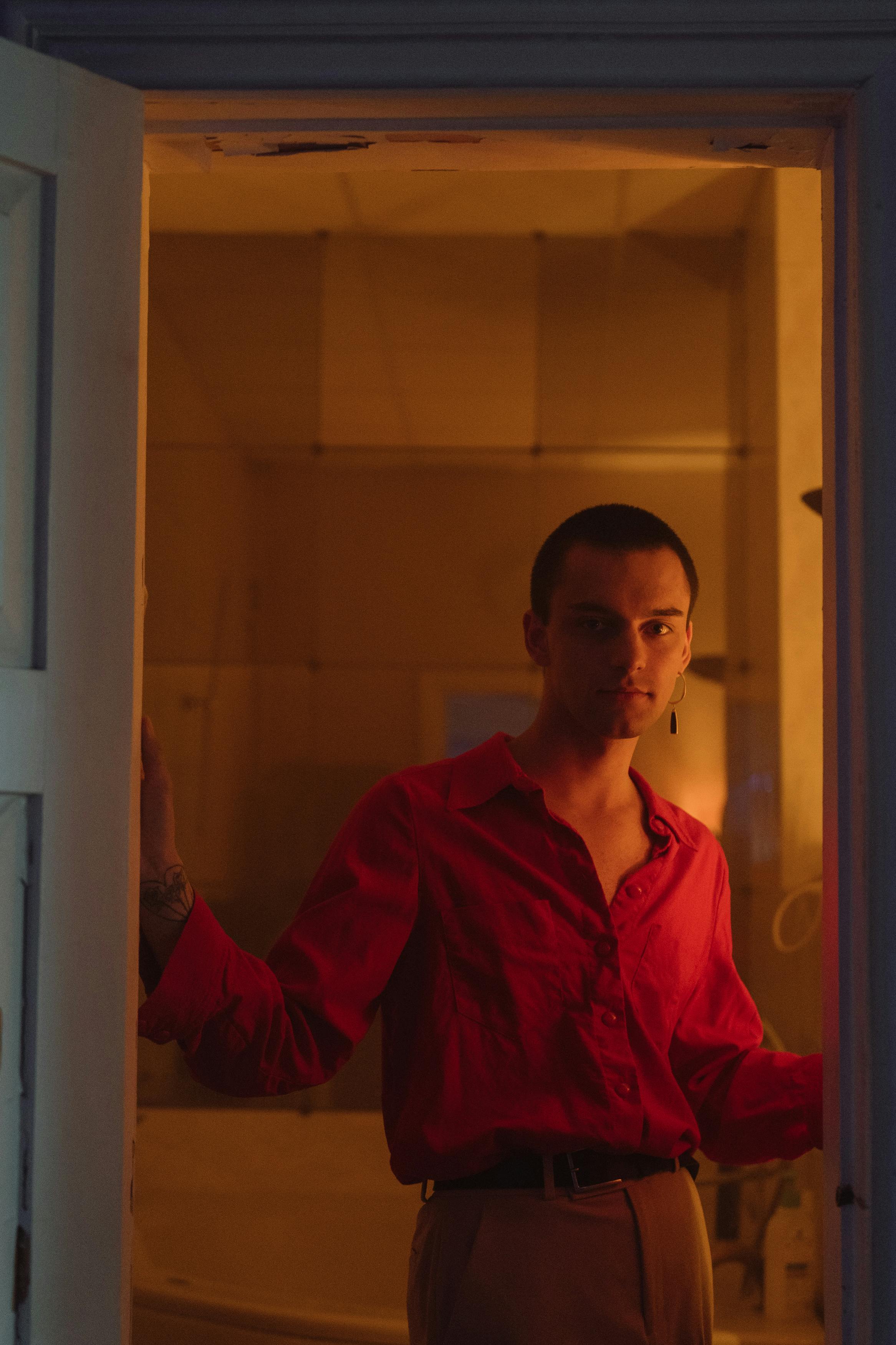灯光温暖的室内，一名穿着红色衬衫、戴着耳环的男子肖像矗立着