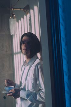在柔和的灯光下，一位兼具男女双性气质的男人手持茶杯，优雅与微妙在他身上融为一体