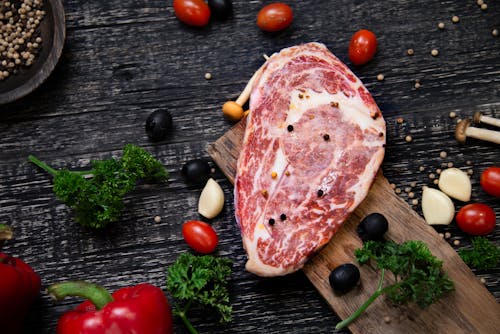 Free Raw Meat on Cutting Board and Vegetables on Wooden Table Stock Photo