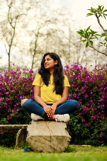 A cheerful woman sits on a bench in a lush Munnar garden, surrounded by vibrant purple flowers.