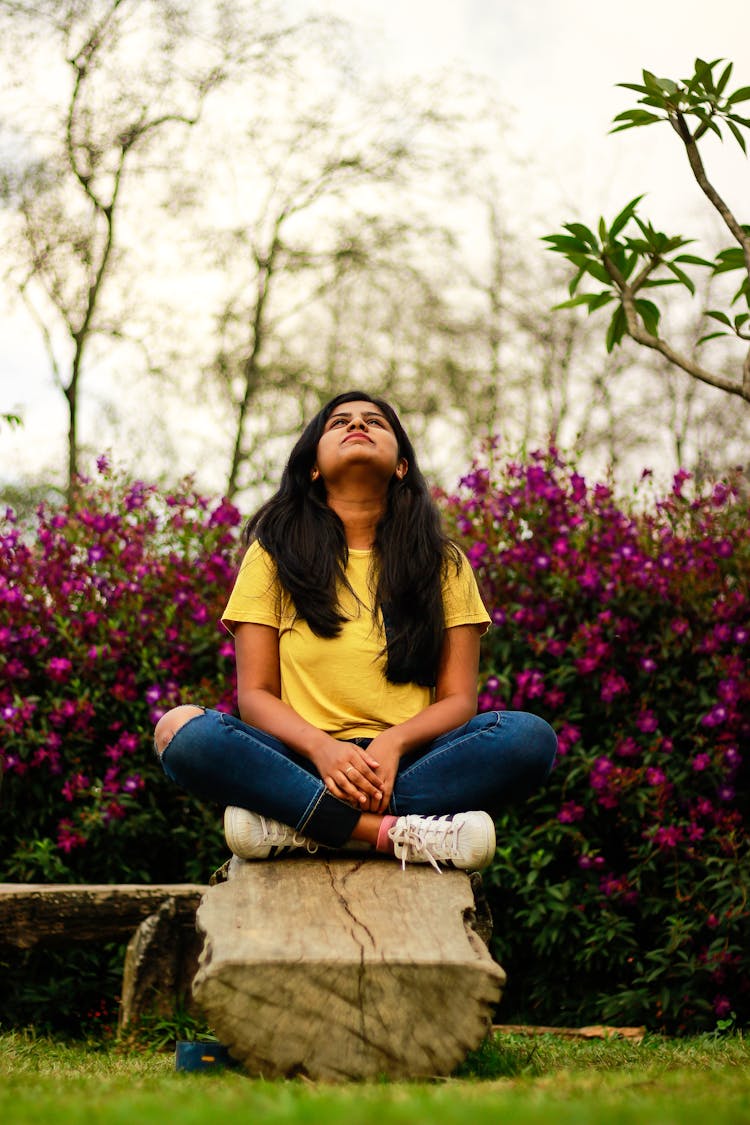 Woman Sitting In Lotus Pose On Rock In Garden