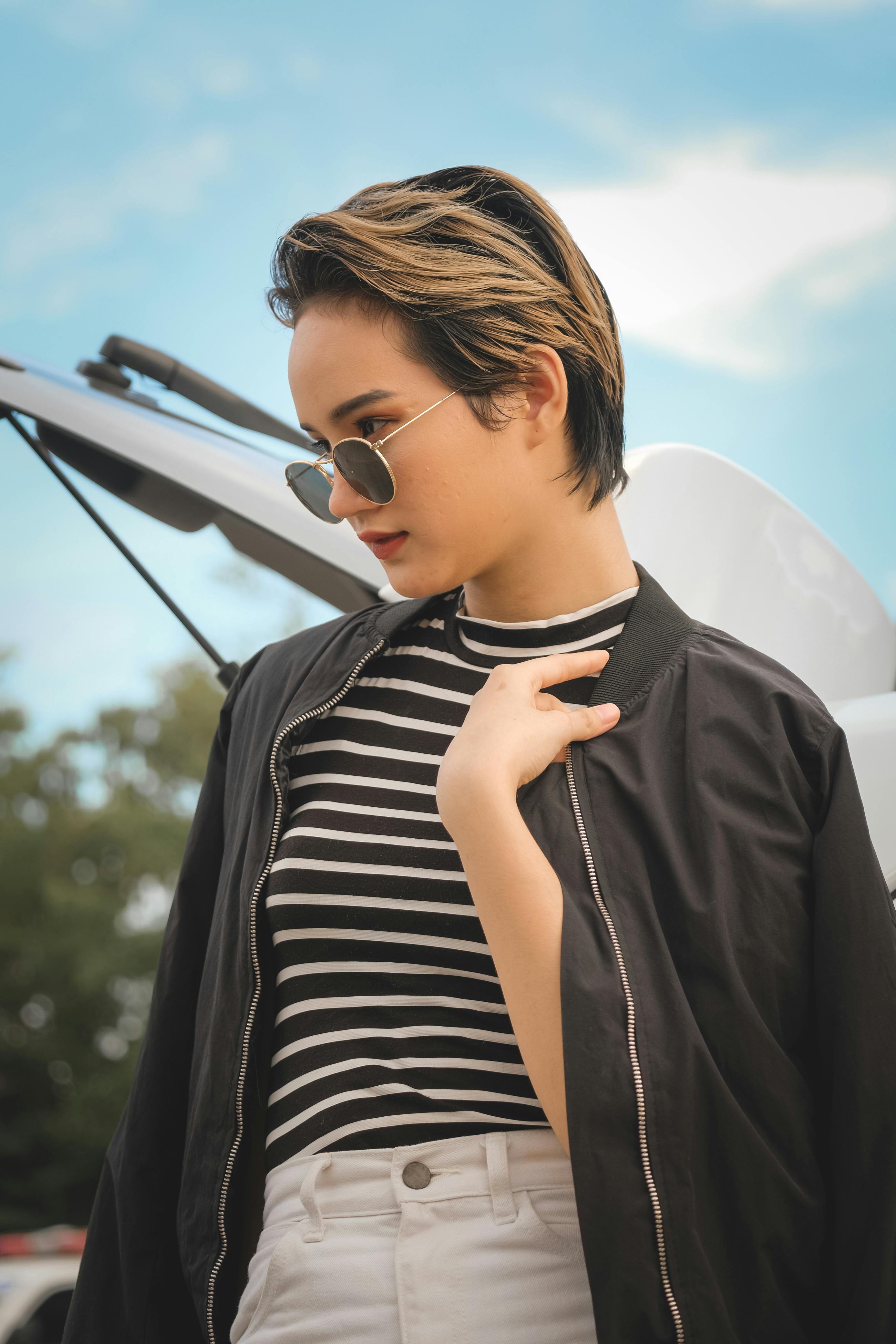 A fashionable young woman with short hair and sunglasses enjoys a sunny day outdoors.