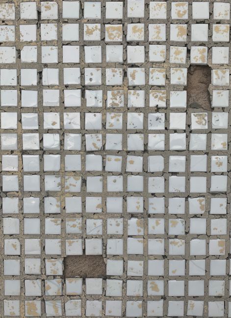 Close-up view of a worn mosaic tile pattern with missing pieces, creating an abstract texture.