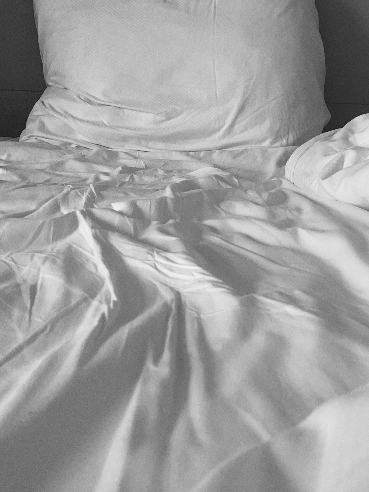 White pillow and rumpled white satin bedding in soft light