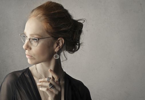 A graceful caucasian woman wearing eyeglasses and jewelry in a sophisticated headshot.