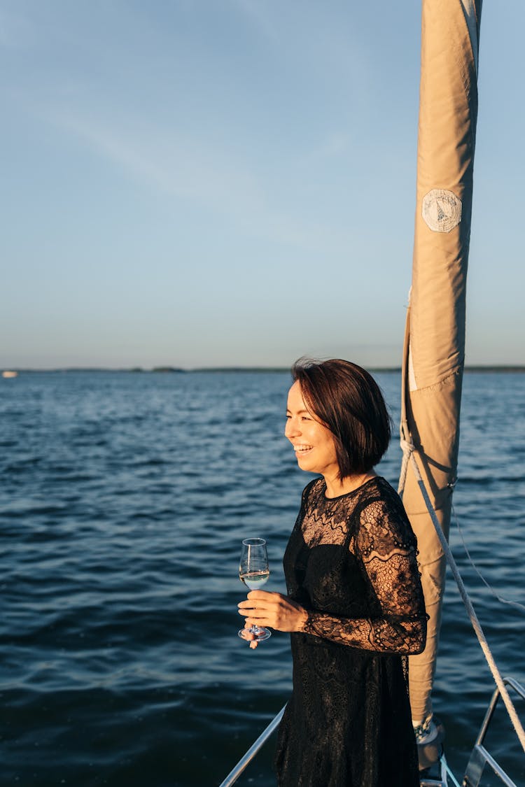 A Woman In Black Lace Dress Standing On A Sailing Boat While Holding A Wine Glass