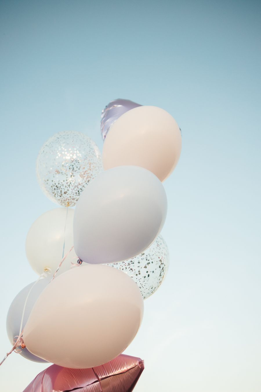 Pastel balloons floating under a clear blue sky