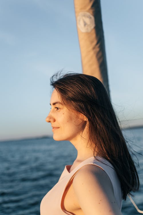 Side View of a Young Woman Standing in Sunlight on the Background of the Sea