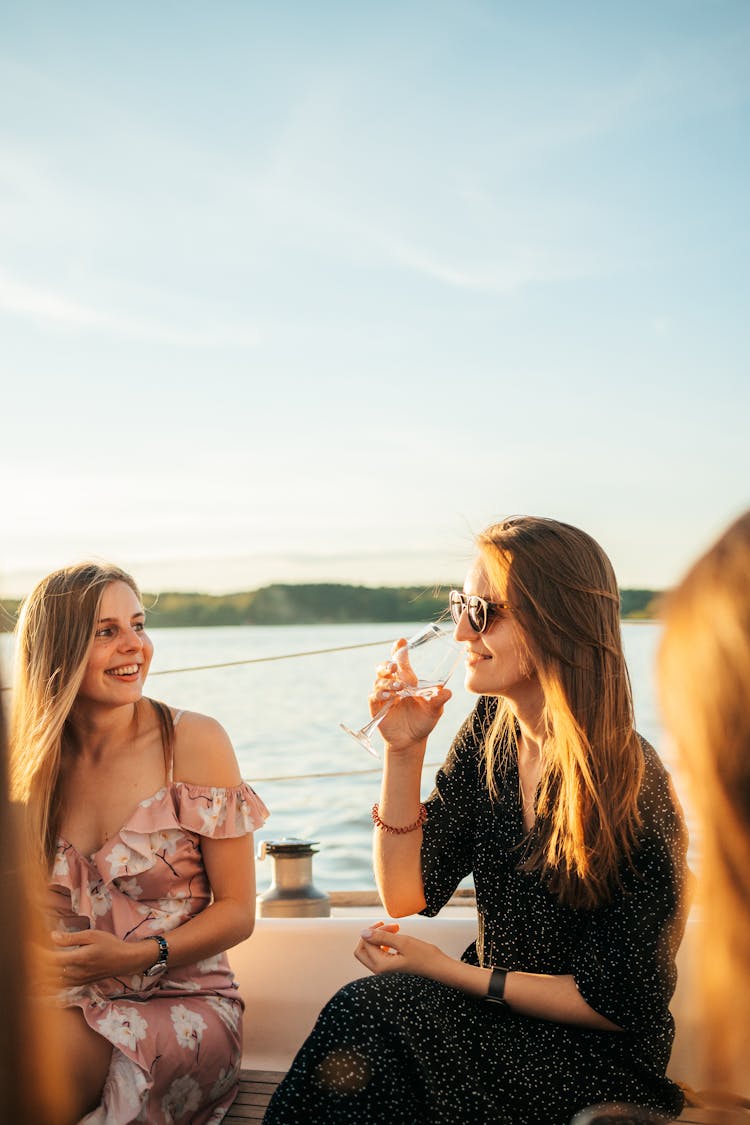 A Woman In Floral Dress Sitting Beside The Woman In Black Dress Drinking Wine