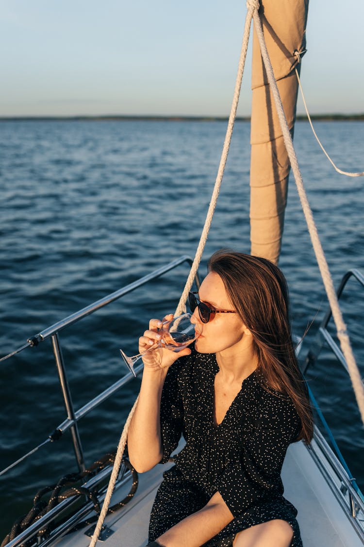 A Woman In Black Dress Sitting On The Boat While Drinking Wine