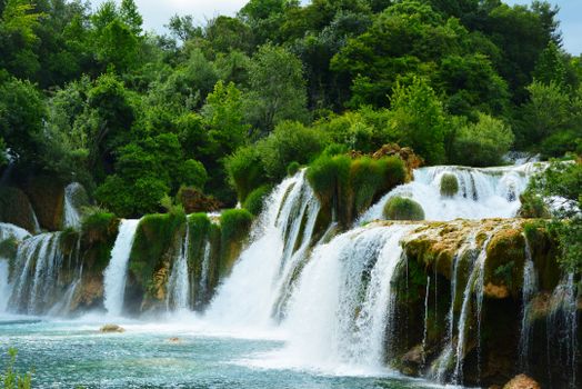 Beautiful waterfall cascading through lush green trees in a vibrant summer landscape.