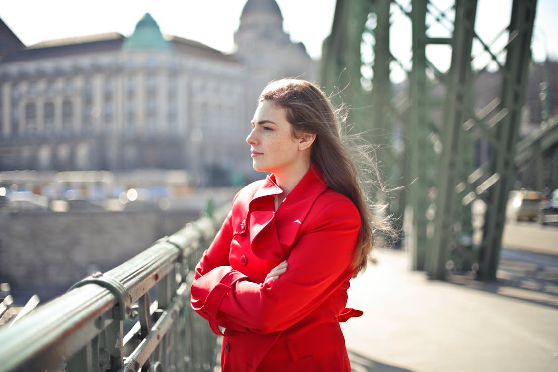 A Woman in Red Coat Standing on the Bridge with Her Arms Crossed