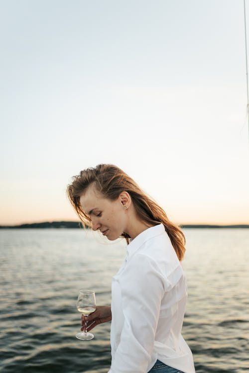 Woman in White Long Sleeve Shirt Standing Near Body of Water