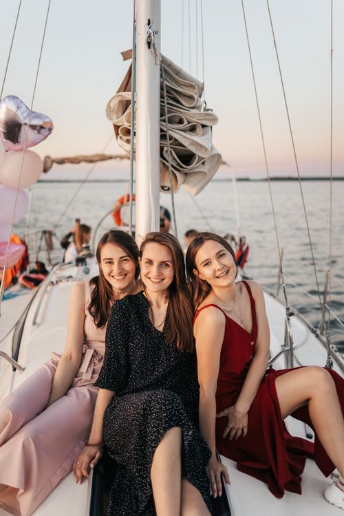 Free Three women in dresses enjoying a relaxing sailboat ride at sea during sunset. Stock Photo