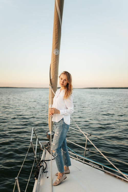 Woman in White Long Sleeve Shirt and Blue Denim Jeans Standing on Boat