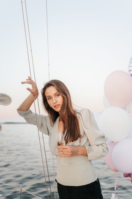 Woman holding champagne glass on yacht with balloons, enjoying a peaceful evening at sea.