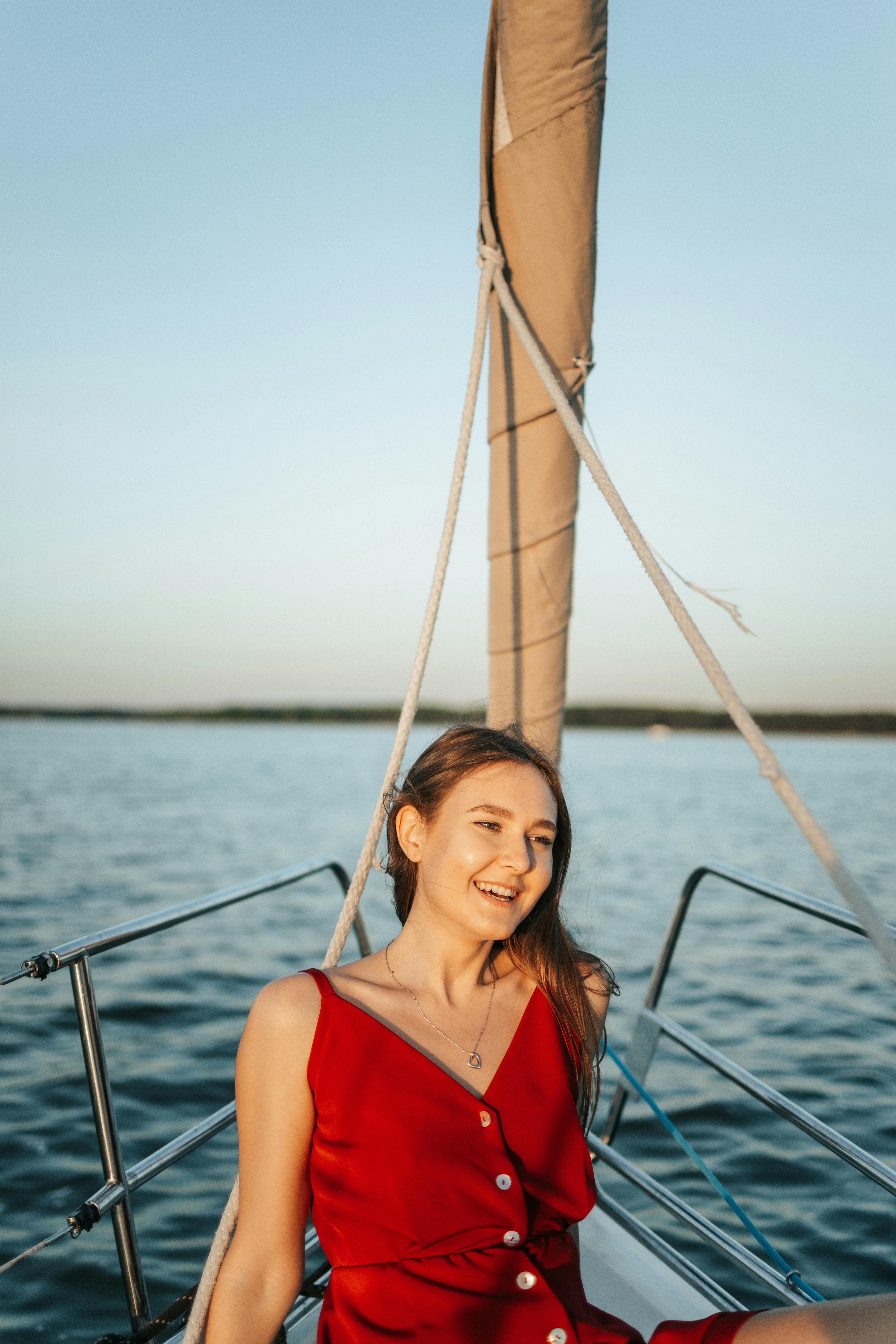白天，天空晴朗，一名身穿红色连衣裙的女子在帆船上微笑