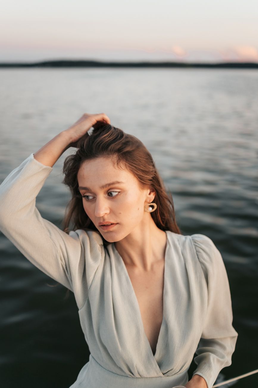 Serene portrait of a woman posing by a calm lake during twilight, capturing tranquility and grace.