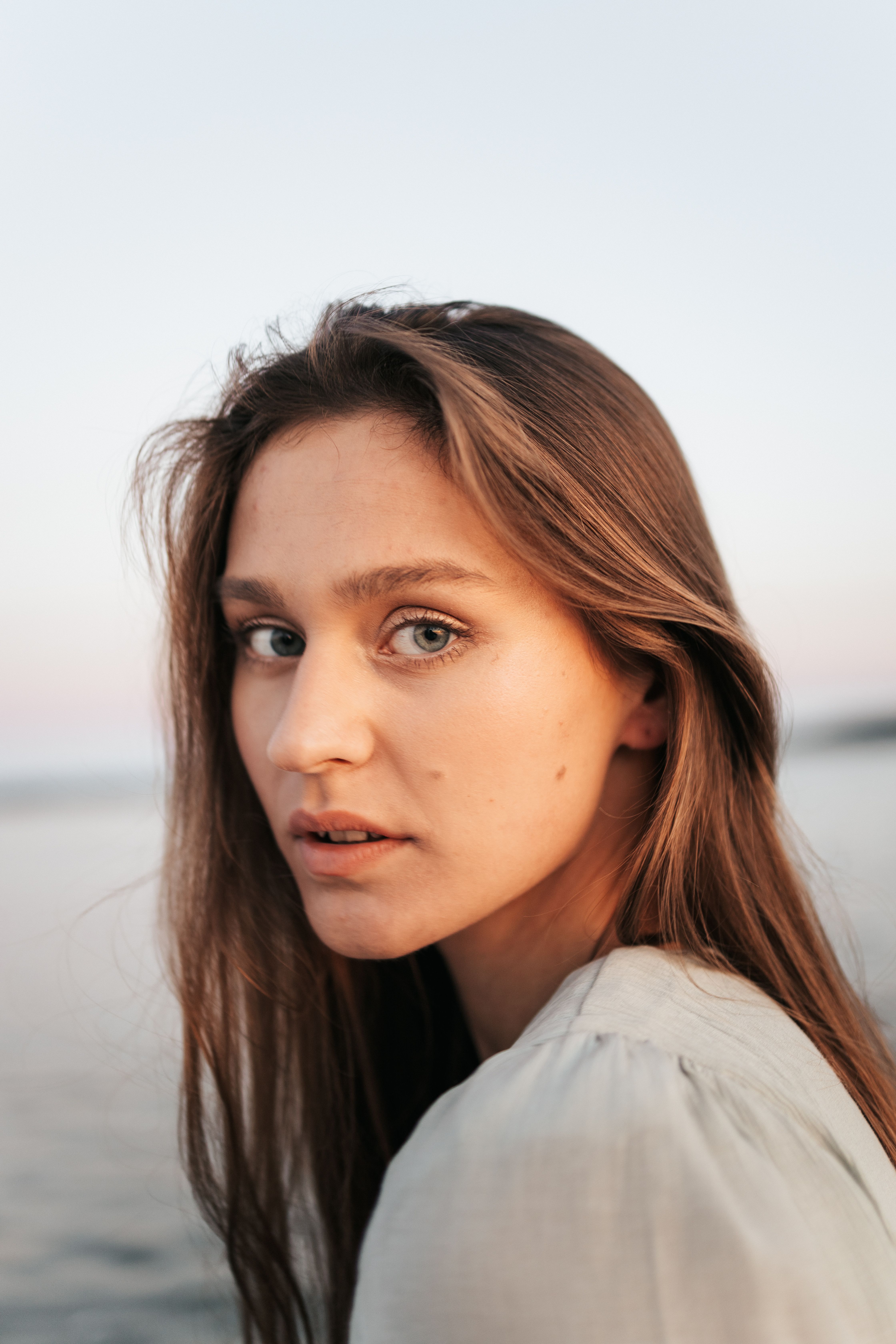 A serene portrait of a woman with long hair by the sea at dusk, capturing a peaceful moment.