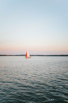 一艘孤独的帆船滑翔在平静的海面上，天空柔和，日落时分一片宁静
