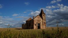 Exterior of ruined medieval church with remaining masonry walls and crosses on top located on spacious grassy valley