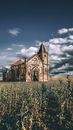 Exterior of ancient desolated masonry church abandoned on grassy vast lawn in remote countryside