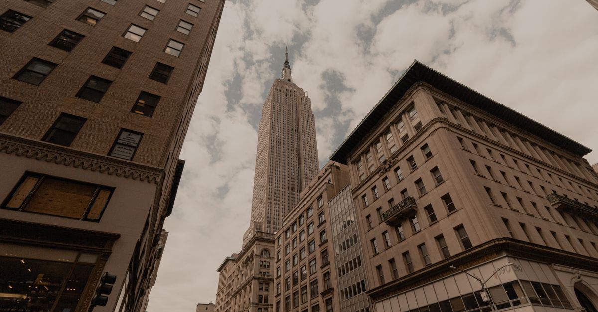 Dramatic urban cityscape featuring the iconic Empire State Building in NYC against a cloudy sky.