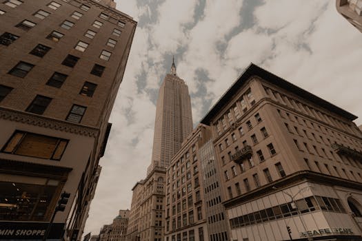 Dramatic urban cityscape featuring the iconic Empire State Building in NYC against a cloudy sky.