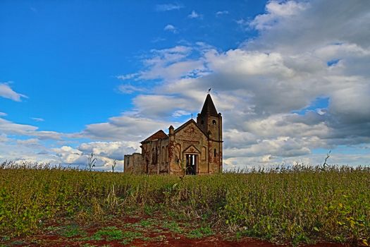 Ground level of abandoned stone church located in green grassy field against cloudy blue sky in Palmital