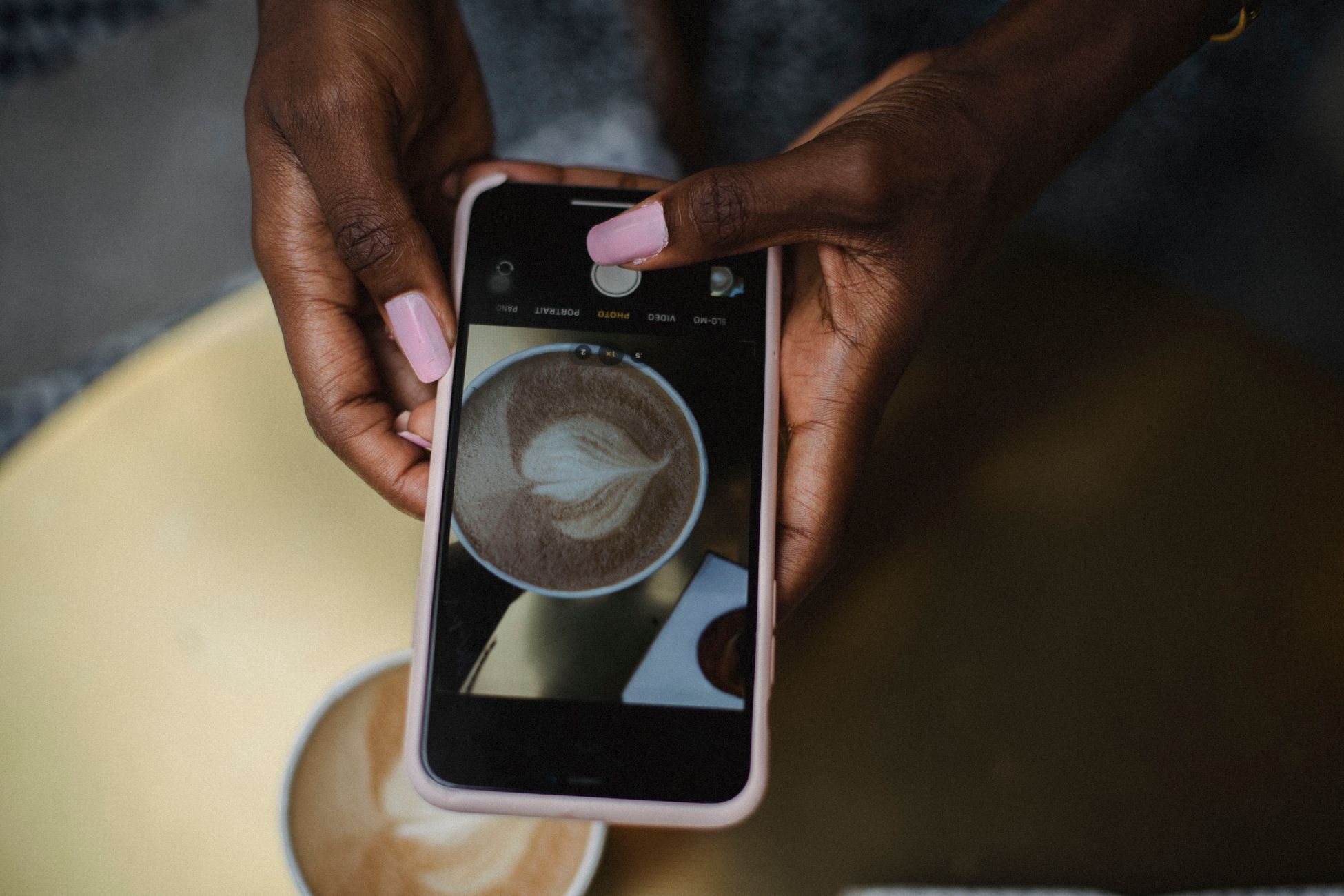 A person photographing a latte with unique art using a smartphone.