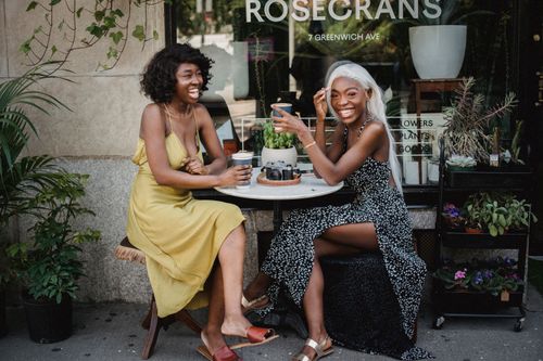 Free Two friends share laughter over coffee at a charming sidewalk cafe, capturing leisure and joy. Stock Photo