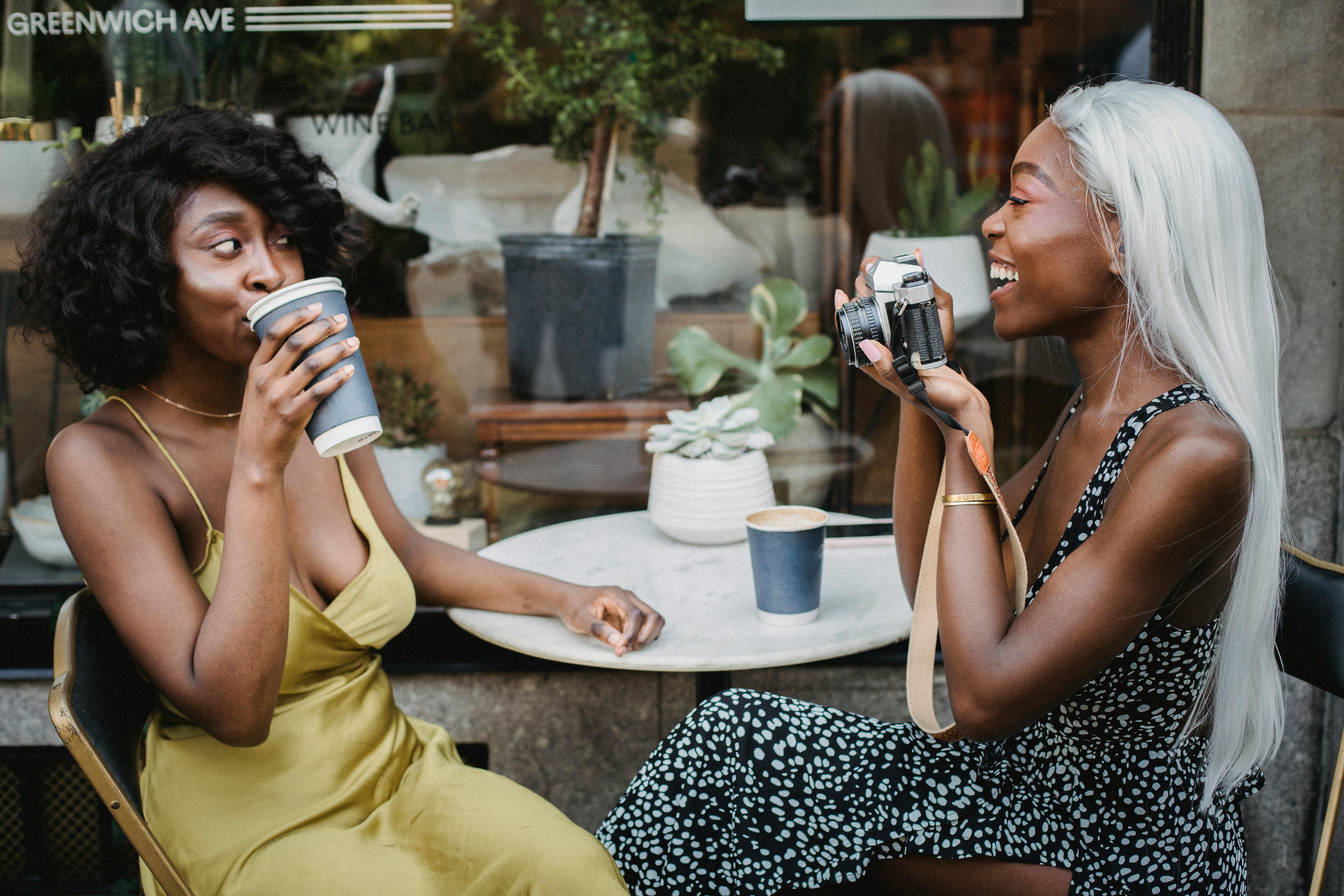 两名女子在咖啡馆里，一边享用咖啡，一边拍照，轻松的氛围和友谊在户外被捕捉下来
